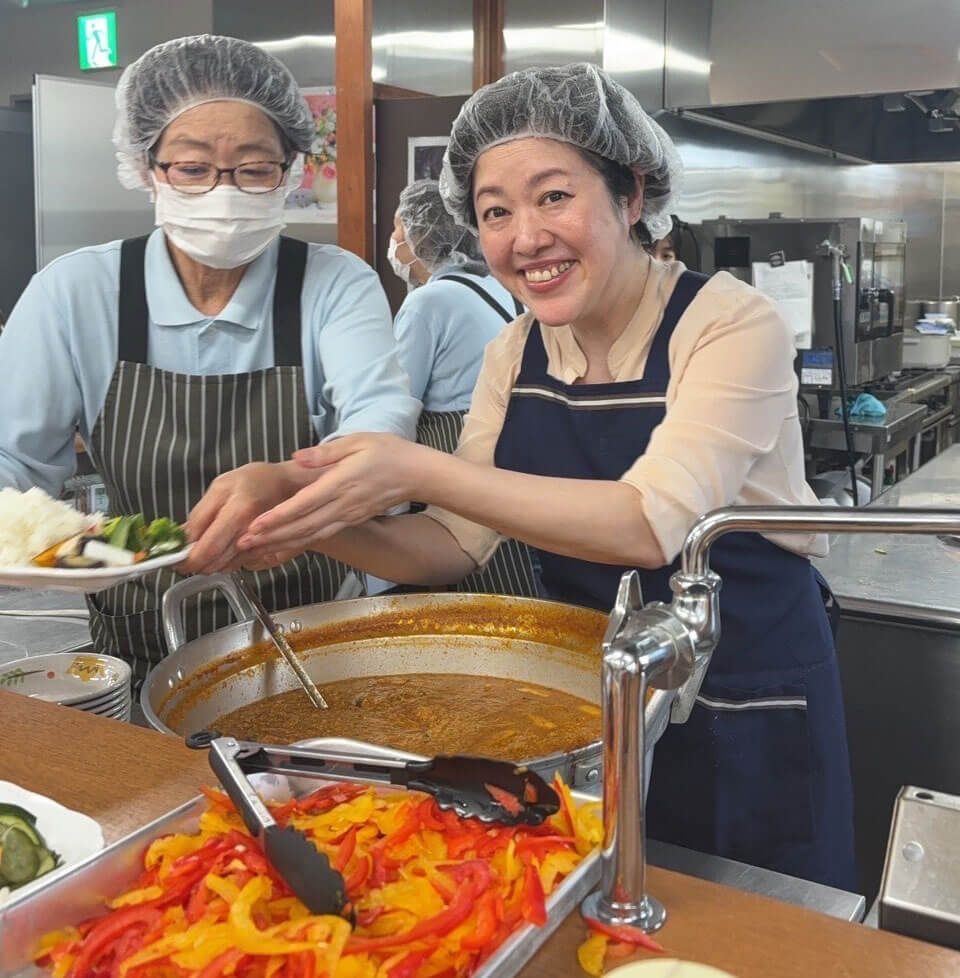 中部第一輸送の社員食堂でキーマカレーを盛り付けるスタッフと講師の小平先生の笑顔