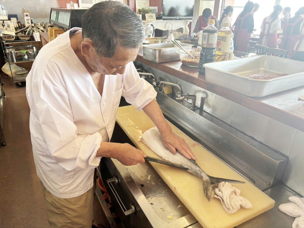 中部第一輸送の会長が魚をさばいて料理を指導している様子