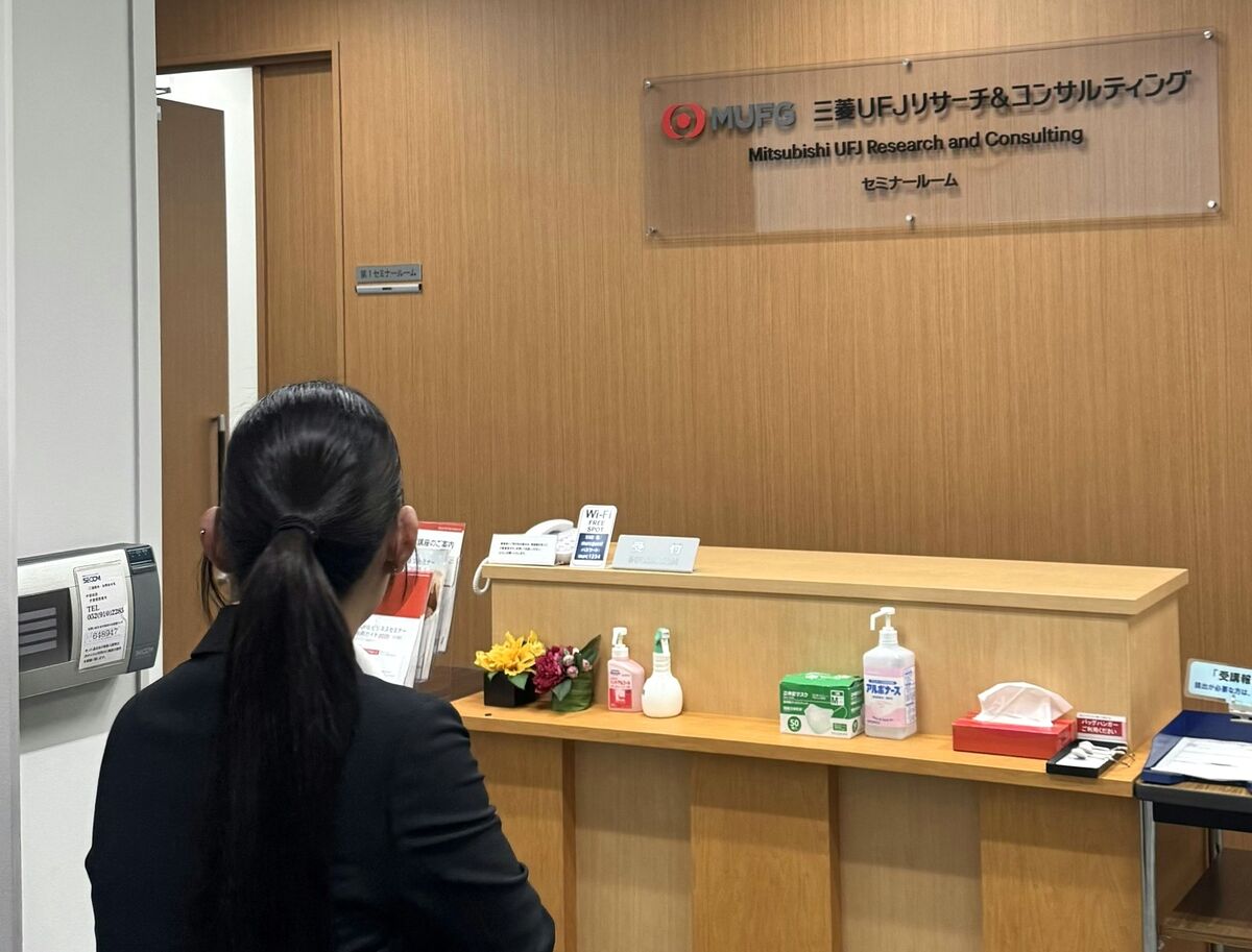 三菱UFJリサーチ＆コンサルティングのセミナー受付の前に立つ中部第一グループの新入社員