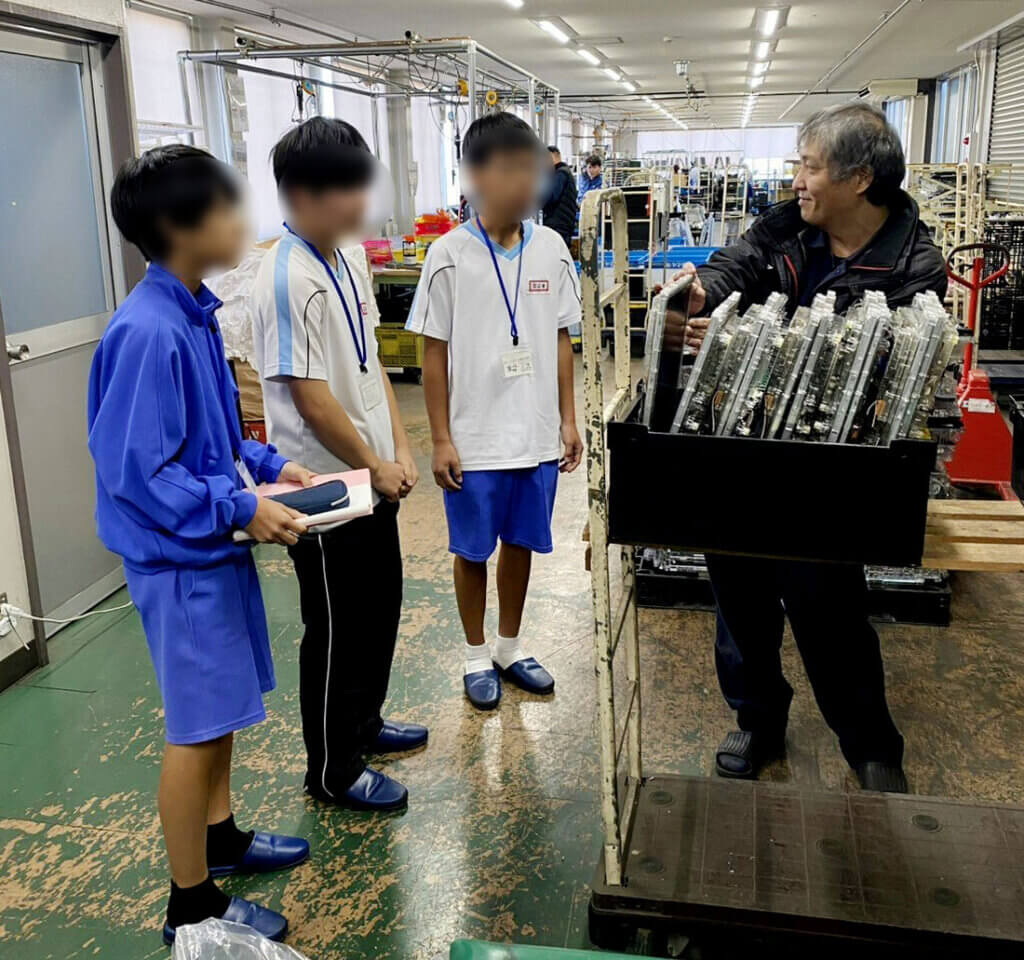 中部第一輸送の倉庫内で流通加工について説明を受ける蟹江中学校の生徒。社員が製品を手に取りながら丁寧に解説している