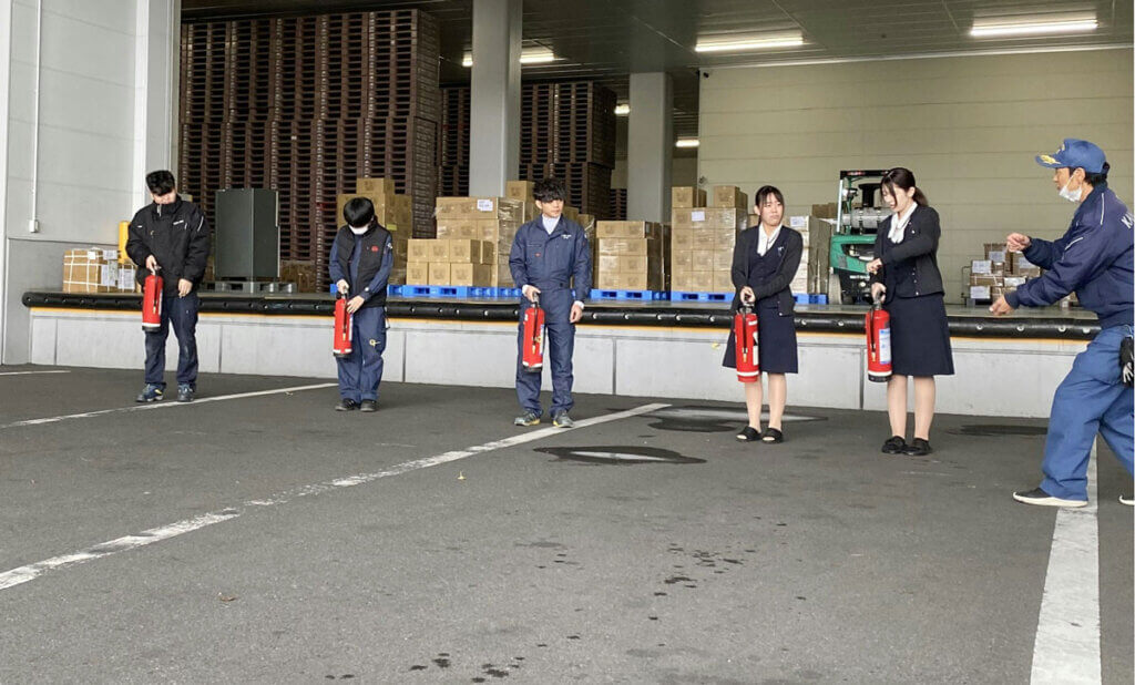 中部第一グループの倉庫内で、消火器を手に持ち実践訓練に参加する社員たち(2025年12月)