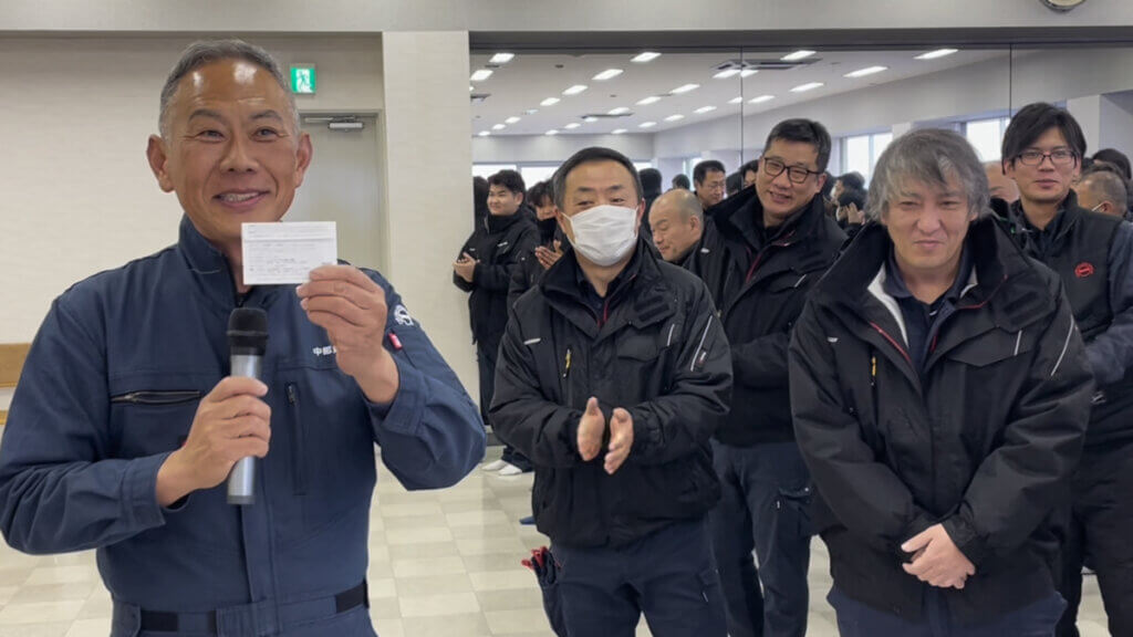 中部第一輸送の仕事始め式で表彰を受ける社員。笑顔で賞状を掲げる姿と同僚たちの温かい拍手