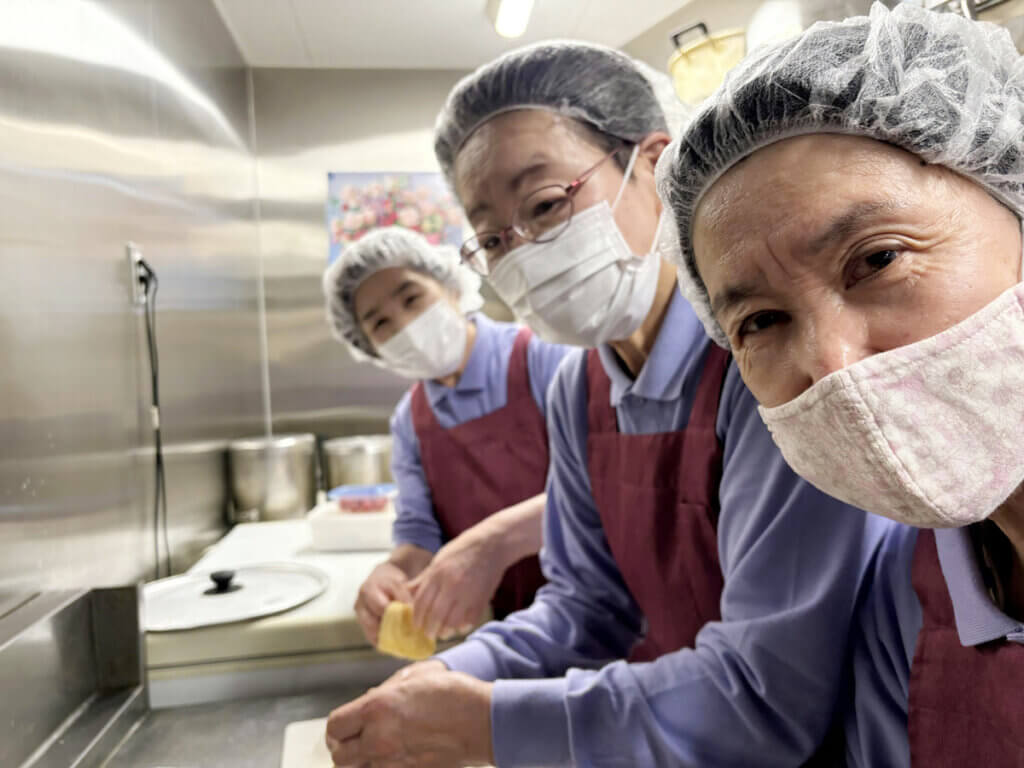 食堂スタッフが声をかけ合いながら調理を進める様子