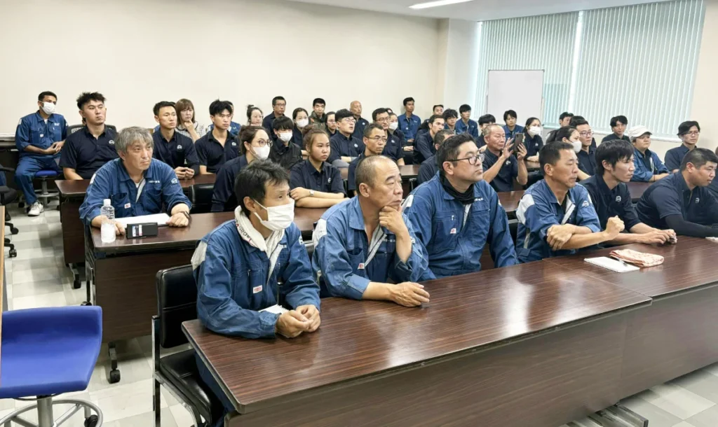 会議室いっぱいに多くのスタッフが集まり、真剣な表情で説明に耳を傾けている